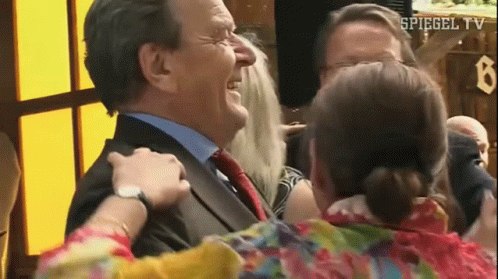 A Man In A Suit And Tie Is Being Hugged By A Woman In A Floral Shirt . GIF
