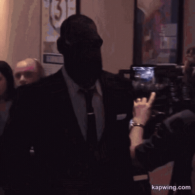 A Man In A Suit And Tie Is Being Photographed By A Woman With The Website Kapwing.com Visible GIF