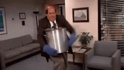 A Man In A Suit And Tie Is Carrying A Large Pot Of Food In A Living Room . GIF