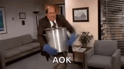A Man In A Suit And Tie Is Carrying A Pot In A Living Room . GIF