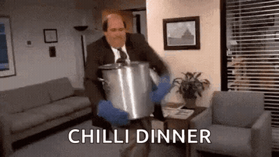 A Man In A Suit And Tie Is Carrying A Pot Of Chili Dinner In A Living Room . GIF