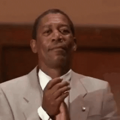 A Man In A Suit And Tie Is Clapping His Hands In A Courtroom . GIF