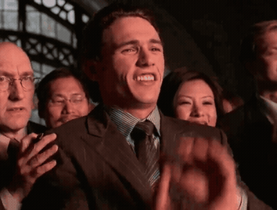 A Man In A Suit And Tie Is Clapping His Hands In A Crowd GIF