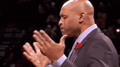 A Man In A Suit And Tie Is Clapping His Hands In A Crowd . GIF