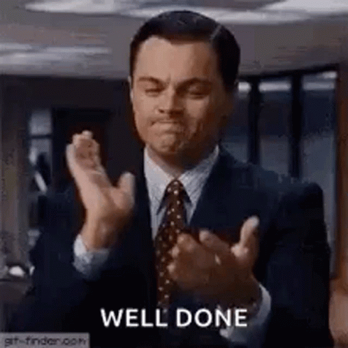 A Man In A Suit And Tie Is Clapping His Hands In A Room . GIF