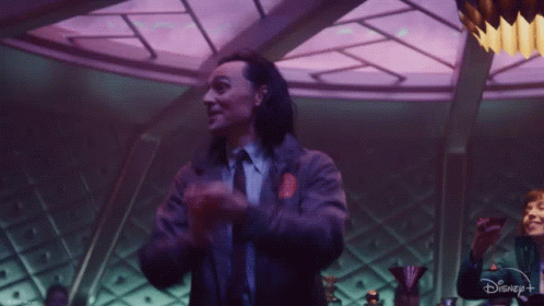 A Man In A Suit And Tie Is Clapping His Hands In A Room With Purple Lights . GIF