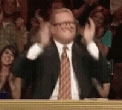 A Man In A Suit And Tie Is Clapping His Hands In Front Of A Crowd Of People . GIF