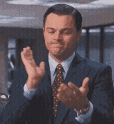 A Man In A Suit And Tie Is Clapping His Hands Together . GIF