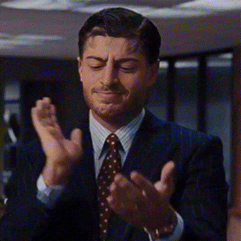 A Man In A Suit And Tie Is Clapping His Hands Together . GIF