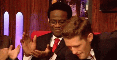 A Man In A Suit And Tie Is Clapping His Hands While Another Man Looks On . GIF