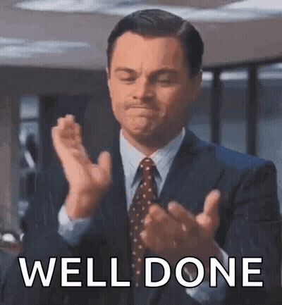 A Man In A Suit And Tie Is Clapping His Hands With The Words `` Well Done '' Behind Him . GIF