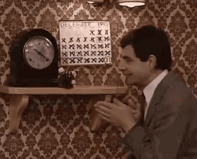 A Man In A Suit And Tie Is Clapping In Front Of A Clock And A Calendar On A Shelf . GIF