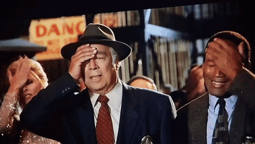 A Man In A Suit And Tie Is Covering His Face In Front Of A Sign That Says Danger GIF
