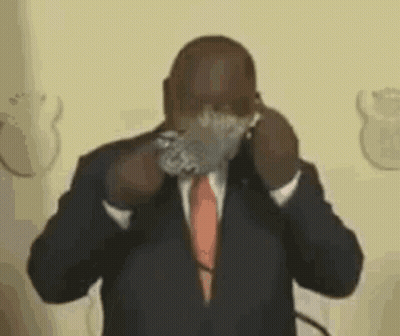 A Man In A Suit And Tie Is Covering His Face With A Piece Of Tape . GIF