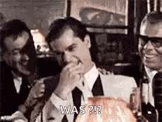A Man In A Suit And Tie Is Covering His Mouth With His Hand While Sitting At A Table . GIF