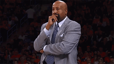 A Man In A Suit And Tie Is Covering His Mouth With His Hand While Standing On A Basketball Court . GIF