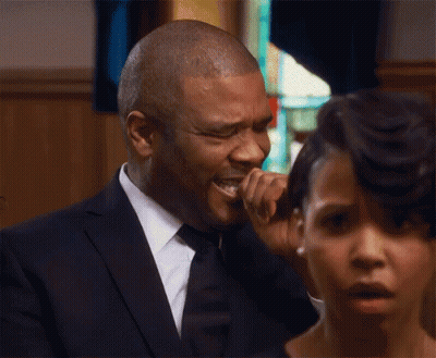 A Man In A Suit And Tie Is Crying At A Funeral While A Woman Looks On . GIF