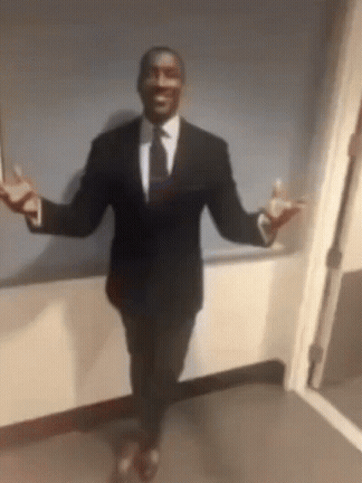A Man In A Suit And Tie Is Dancing In A Hallway GIF