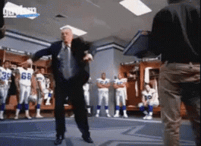 A Man In A Suit And Tie Is Dancing In A Locker Room With Football Players In The Background GIF