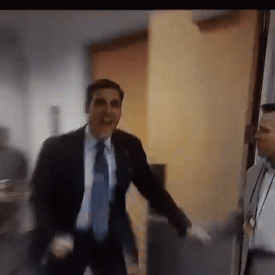 A Man In A Suit And Tie Is Dancing In A Room While Another Man Watches . GIF