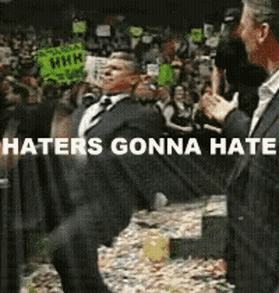 A Man In A Suit And Tie Is Dancing In Front Of A Crowd With The Words Haters Gonna Hate Below Him GIF
