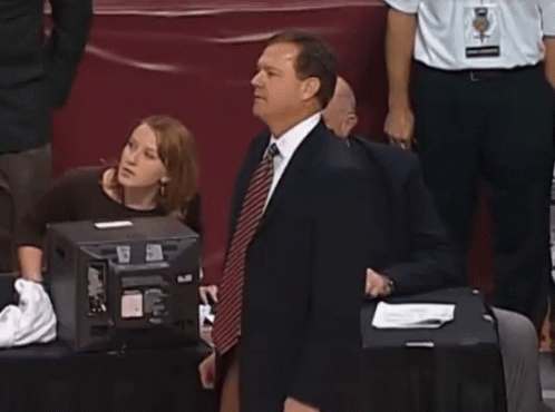 A Man In A Suit And Tie Is Dancing In Front Of A Group Of People GIF