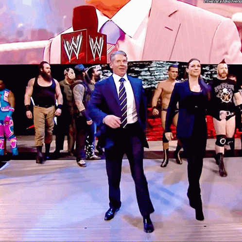 A Man In A Suit And Tie Is Dancing In Front Of A Sign That Says Wwe GIF