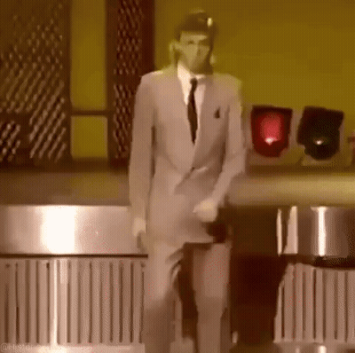 A Man In A Suit And Tie Is Dancing On A Stage In A Dark Room . GIF