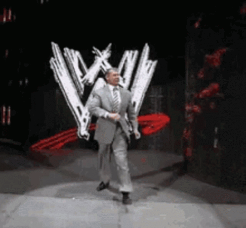 A Man In A Suit And Tie Is Dancing On A Stage In Front Of A Wwe Logo . GIF