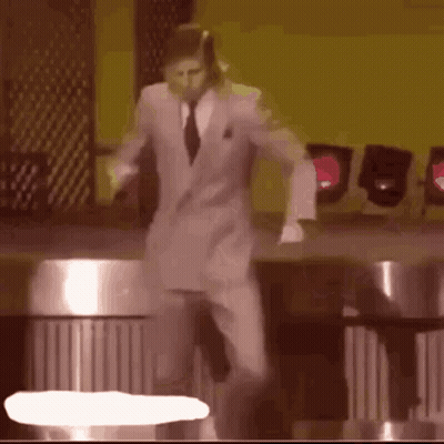 A Man In A Suit And Tie Is Dancing On A Stage In Front Of A Yellow Wall . GIF