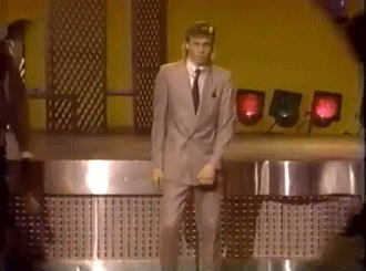 A Man In A Suit And Tie Is Dancing On A Stage With Red Lights Behind Him GIF