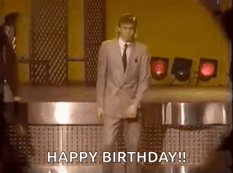 A Man In A Suit And Tie Is Dancing On A Stage With The Words `` Happy Birthday '' . GIF