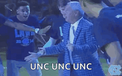A Man In A Suit And Tie Is Dancing With A Group Of People In A Circle . GIF