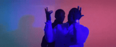 A Man In A Suit And Tie Is Dancing With His Arms In The Air In A Dark Room . GIF