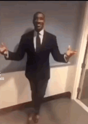 A Man In A Suit And Tie Is Dancing With His Arms Outstretched In A Hallway . GIF