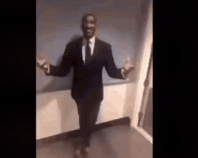 A Man In A Suit And Tie Is Dancing With His Arms Outstretched In A Room . GIF