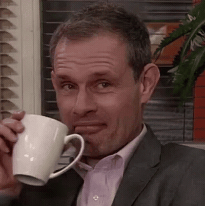 A Man In A Suit And Tie Is Drinking From A White Mug . GIF