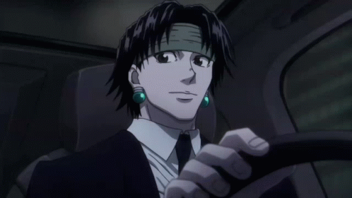 A Man In A Suit And Tie Is Driving A Car With Green Earrings GIF