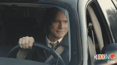A Man In A Suit And Tie Is Driving A Car With The Word Kidding Written On The Side GIF