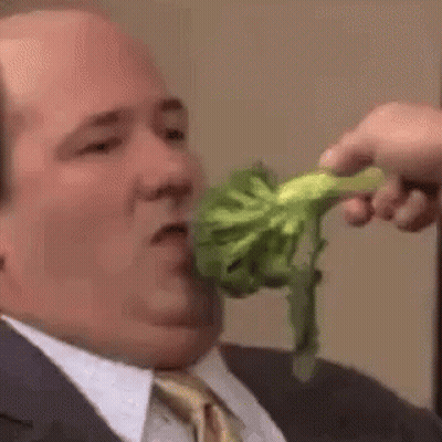 A Man In A Suit And Tie Is Eating Broccoli From A Person 'S Hand . GIF