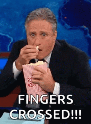 A Man In A Suit And Tie Is Eating Popcorn And Saying `` Fingers Crossed ! '' GIF