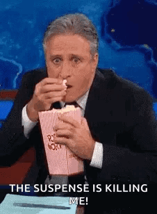 A Man In A Suit And Tie Is Eating Popcorn And Says The Suspense Is Killing Me . GIF