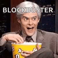 A Man In A Suit And Tie Is Eating Popcorn From A Yellow Bucket . GIF
