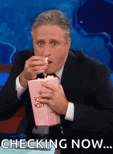 A Man In A Suit And Tie Is Eating Popcorn While Sitting On A Stage . GIF