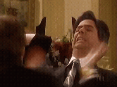 A Man In A Suit And Tie Is Getting Punched In The Face By Another Man . GIF