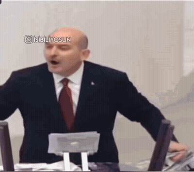 A Man In A Suit And Tie Is Giving A Speech In Front Of A Computer . GIF