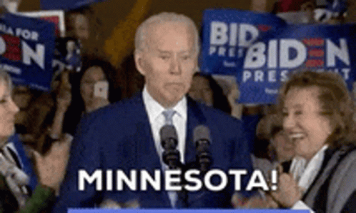 A Man In A Suit And Tie Is Giving A Speech In Front Of A Crowd And Says Minnesota GIF