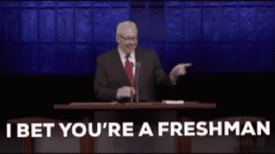 A Man In A Suit And Tie Is Giving A Speech In Front Of A Microphone And Pointing At The Audience . GIF
