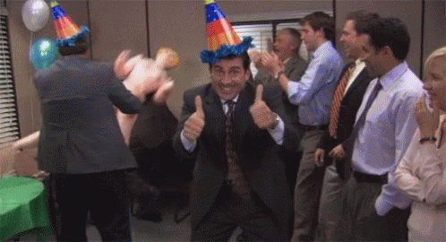 A Man In A Suit And Tie Is Giving A Thumbs Up At A Party While A Group Of People Applaud . GIF