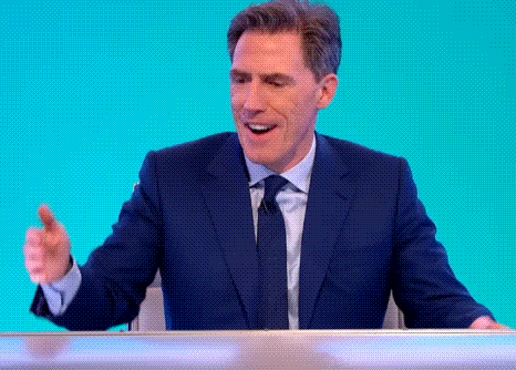 A Man In A Suit And Tie Is Giving A Thumbs Up Sign While Sitting At A Desk . GIF
